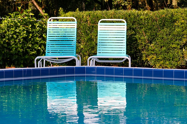 Křišťálově modrý bazén a za ním dvě bílé židličky u živého plotu.jpg